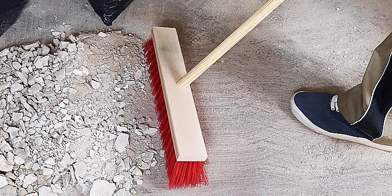 Reinigung von Baustellenresten wie Schutt und Staub mit einem Besen auf einem Betonboden.