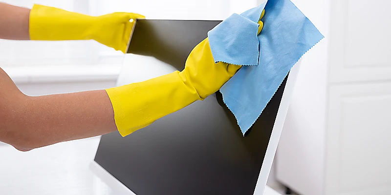 Reinigung eines Computerbildschirms mit Mikrofasertuch und gelben Handschuhen im Büro.